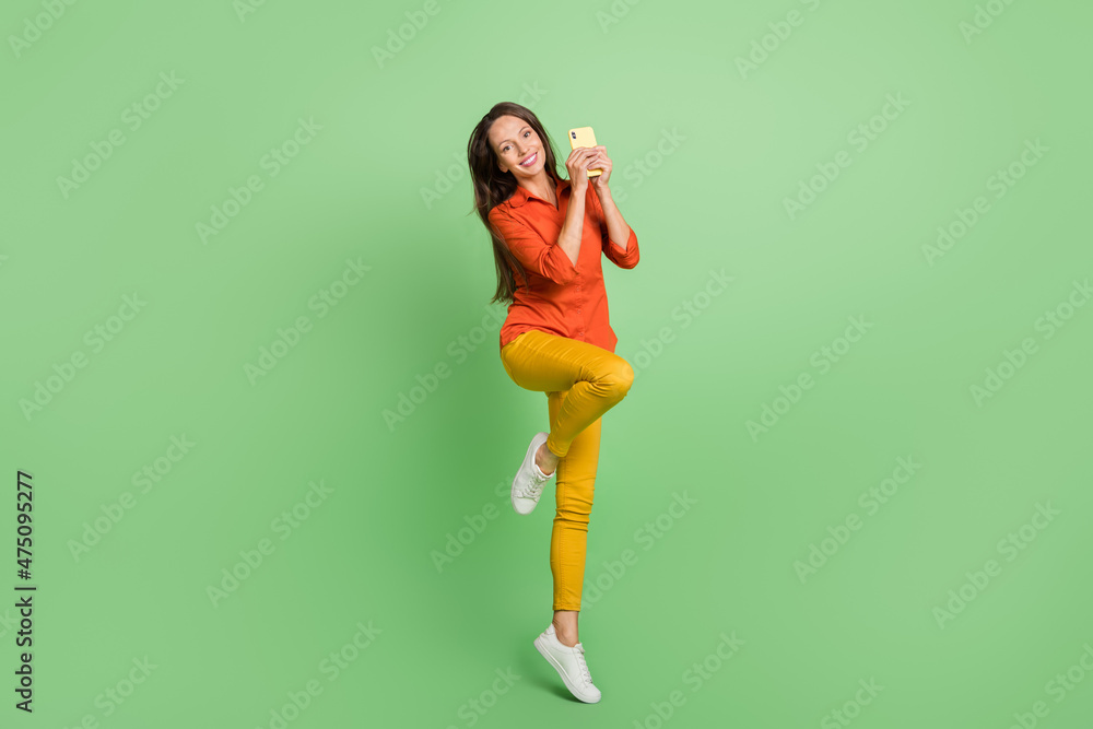 Photo of funny sweet young woman wear red shirt smiling jumping high chatting modern gadget isolated green color background Photo of funny sweet young woman wear red shirt smiling jumping high chatting modern gadget isolated green color background