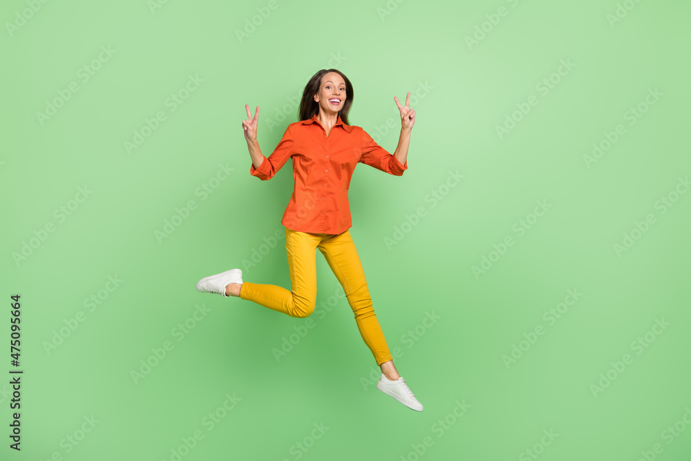 Full length photo of cheerful mature lady show fingers v-symbol jumper isolated over green color background Full length photo of cheerful mature lady show fingers v-symbol jumper isolated over green color background