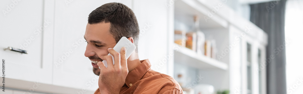 Cheerful man talking on mobile phone in kitchen, banner Cheerful man talking on mobile phone in kitchen, banner