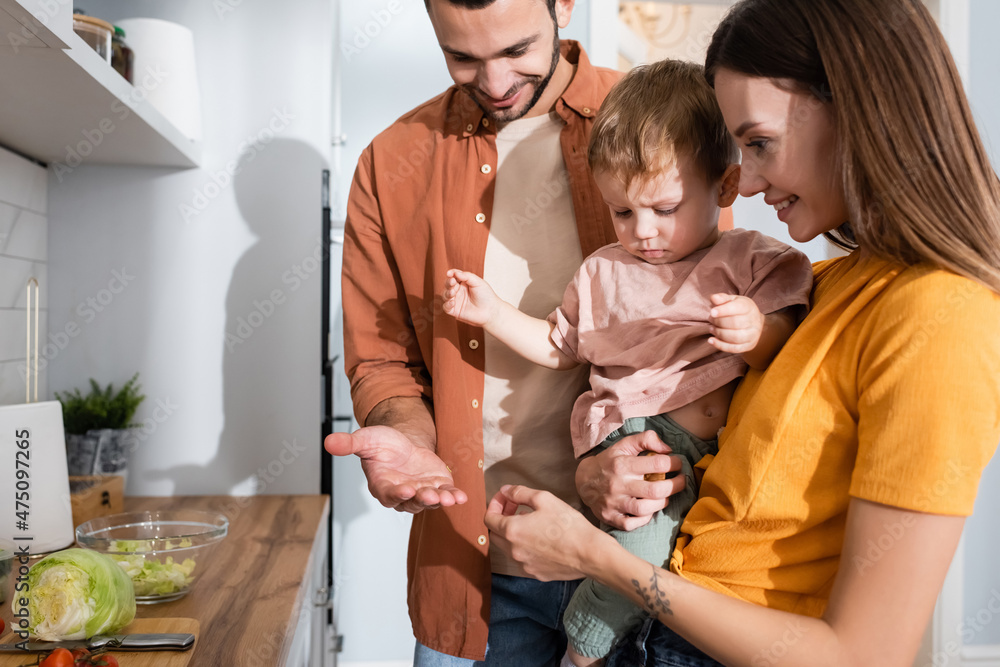 Happy parents looking at kid near vegetables on kitchen worktop Happy parents looking at kid near vegetables on kitchen worktop