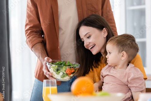 Man holding fresh salad near cheerful wife and son at home