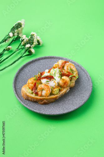 Toast with shrimp, prawns, avocado and poached egg on green background with flowers