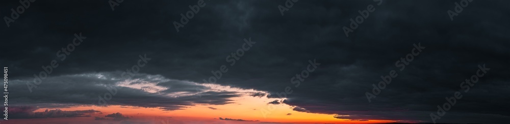 Panorama of dramatic colorful sunset with dark and bright clouds. The sun's rays are breaking through the cloudy sky. Dark clouds against a bright saturated sky.