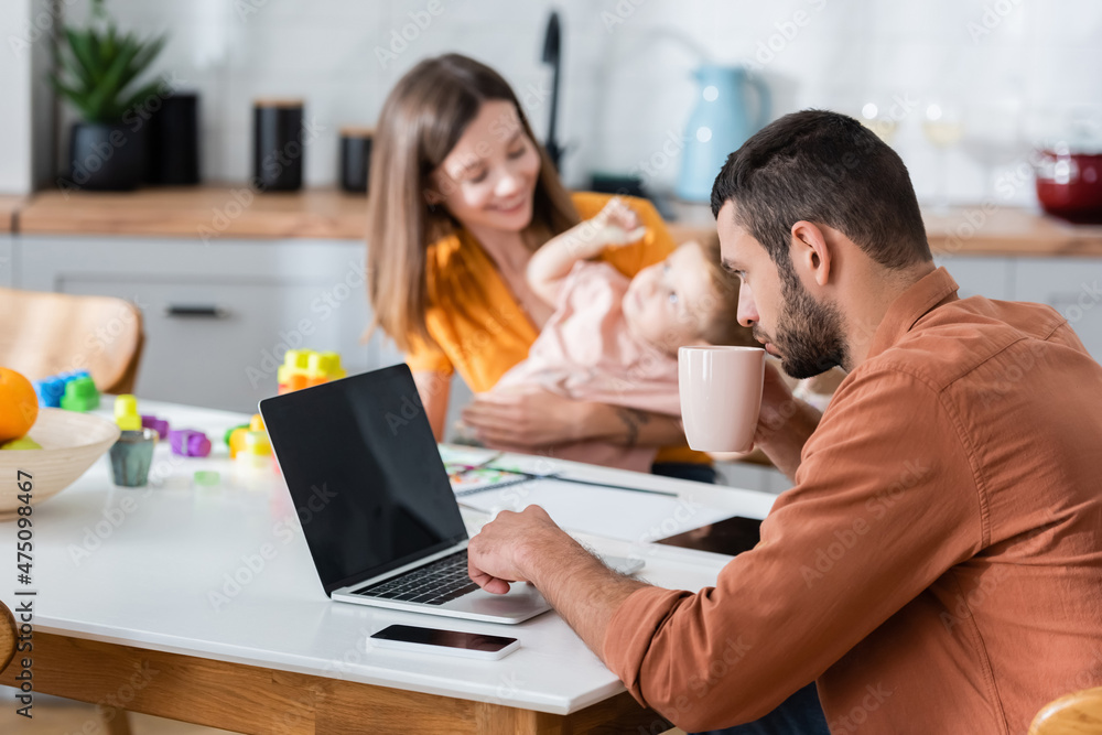 Man holding cup and using laptop near wife and son at home Man holding cup and using laptop near wife and son at home