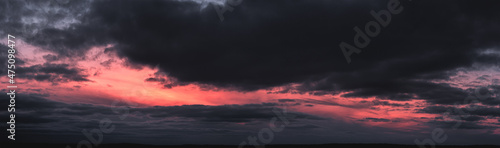 Panorama of dramatic colorful sunset with dark and bright clouds. The sun's rays are breaking through the cloudy sky. Dark clouds against a bright saturated sky.