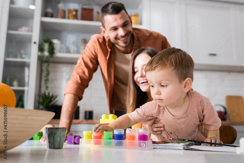 Fototapeta premium Toddler kid taking paint near building blocks and parents at home