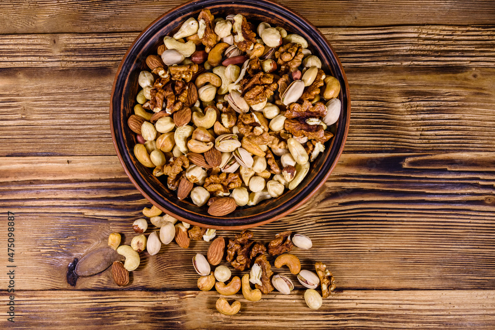 Various nuts (almond, cashew, hazelnut, pistachio, walnut) in ceramic plate on a wooden table. Vegetarian meal. Healthy eating concept. Top view Various nuts (almond, cashew, hazelnut, pistachio, walnut) in ceramic plate on a wooden table. Vegetarian meal. Healthy eating concept. Top view