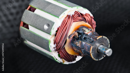 Damaged scorched commutator due to short circuit in rotor winding of DC electric motor. Detail of charred electromotor part with copper wire and metal laminations on blurred black netting background. photo