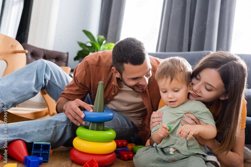 Cheerful parents sitting near son and toys in living room Cheerful parents sitting near son and toys in living room