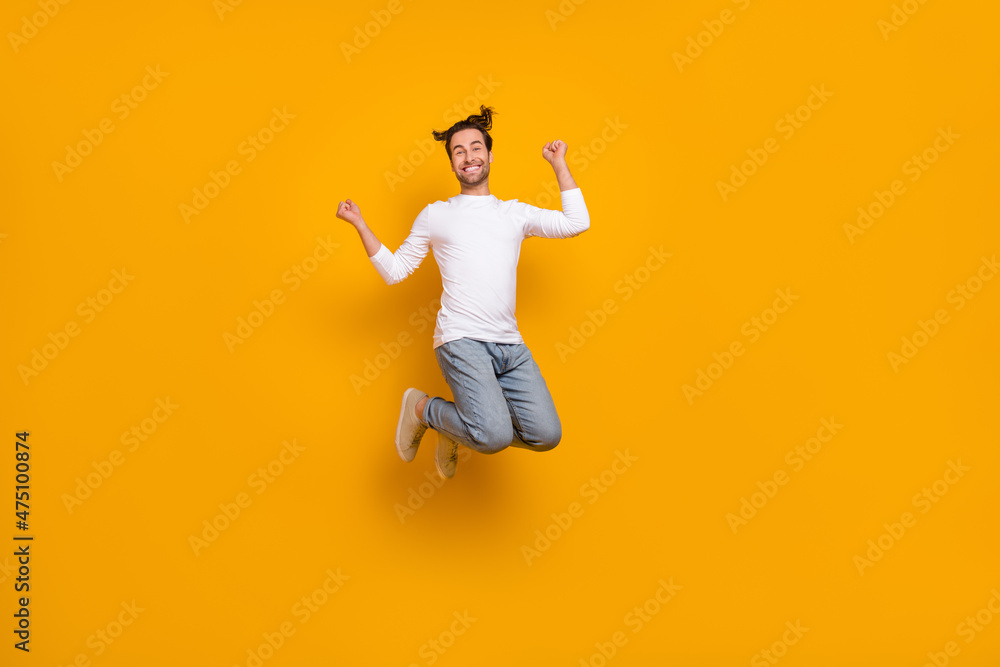 Full length photo of cool brunet young guy jump hands fists wear shirt jeans footwear isolated on yellow background