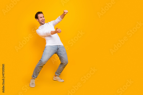 Full length photo of impressed brunet millennial guy drive wear shirt jeans footwear isolated on yellow background