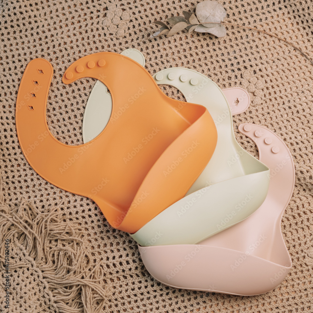 Fototapeta premium Three silicone baby bibs of different colors on beige blanket. Flat lay. Square frame instagram use