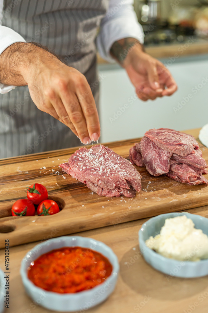 A close-up of a chef adding spices into a piece of meat