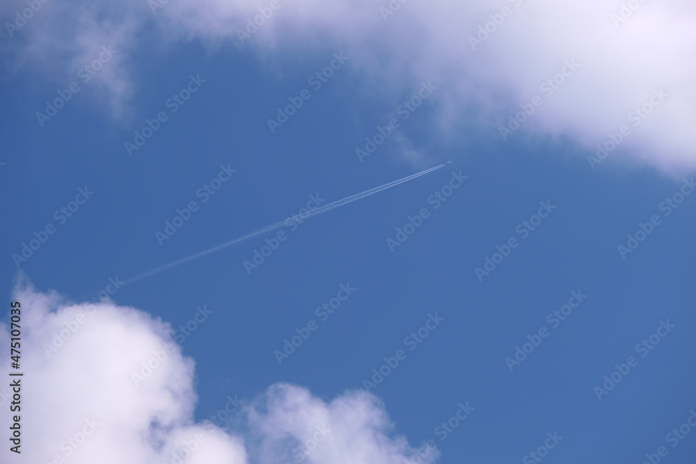 Distant passenger jet plane flying on high altitude on blue sky with white clouds leaving smoke trace of contrail behind. Air traveling concept Distant passenger jet plane flying on high altitude on blue sky with white clouds leaving smoke trace of contrail behind. Air traveling concept