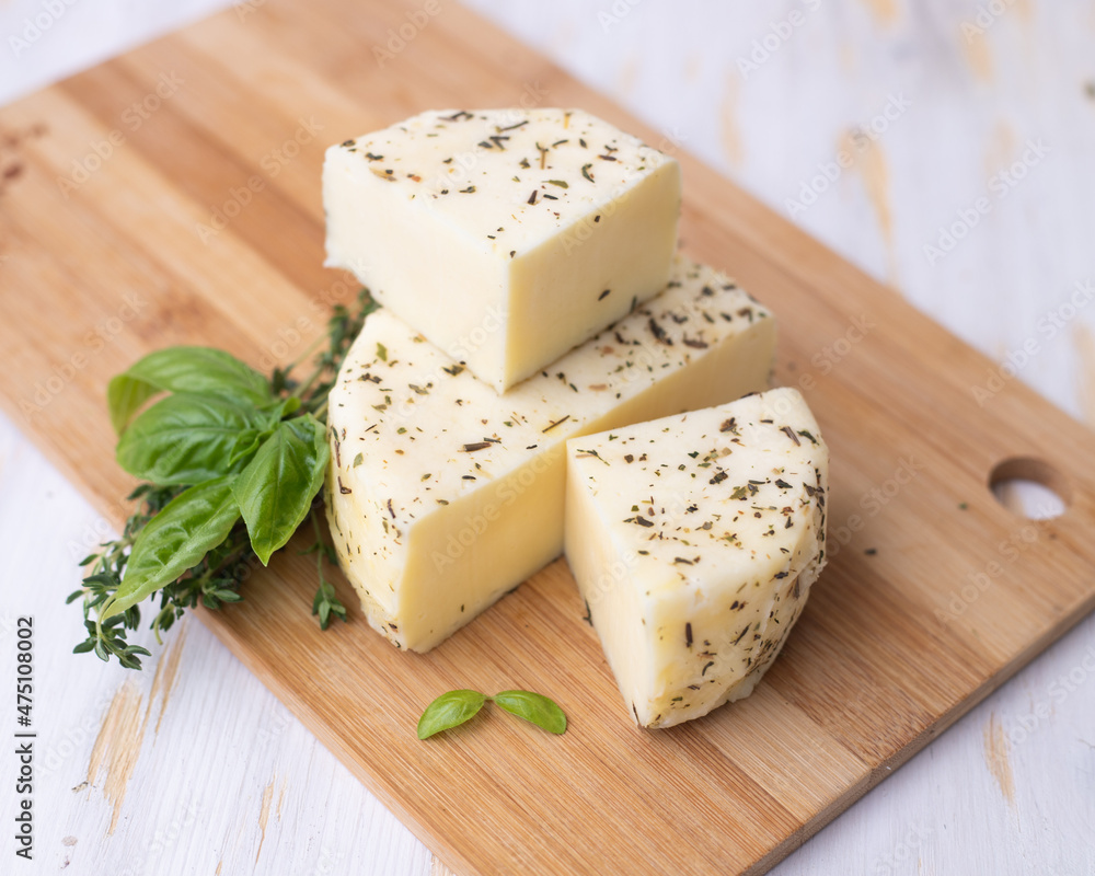 Caciotta cheese lies on a wooden board with basil and thyme.