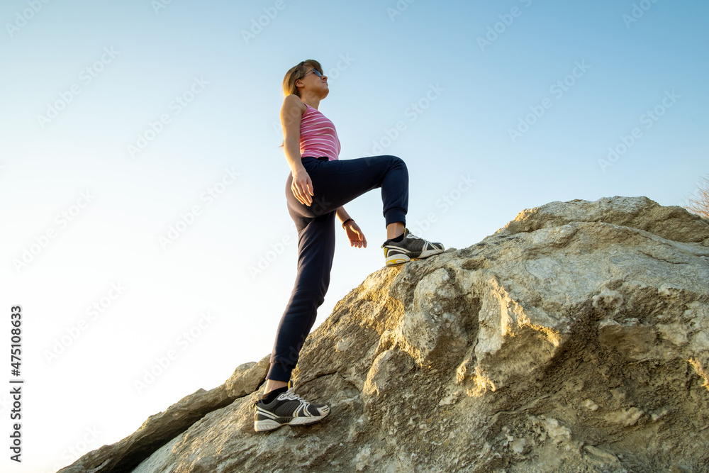 Woman hiker climbing steep big rock on a sunny day. Young female climber overcomes difficult climbing route. Active recreation in nature concept Woman hiker climbing steep big rock on a sunny day. Young female climber overcomes difficult climbing route. Active recreation in nature concept