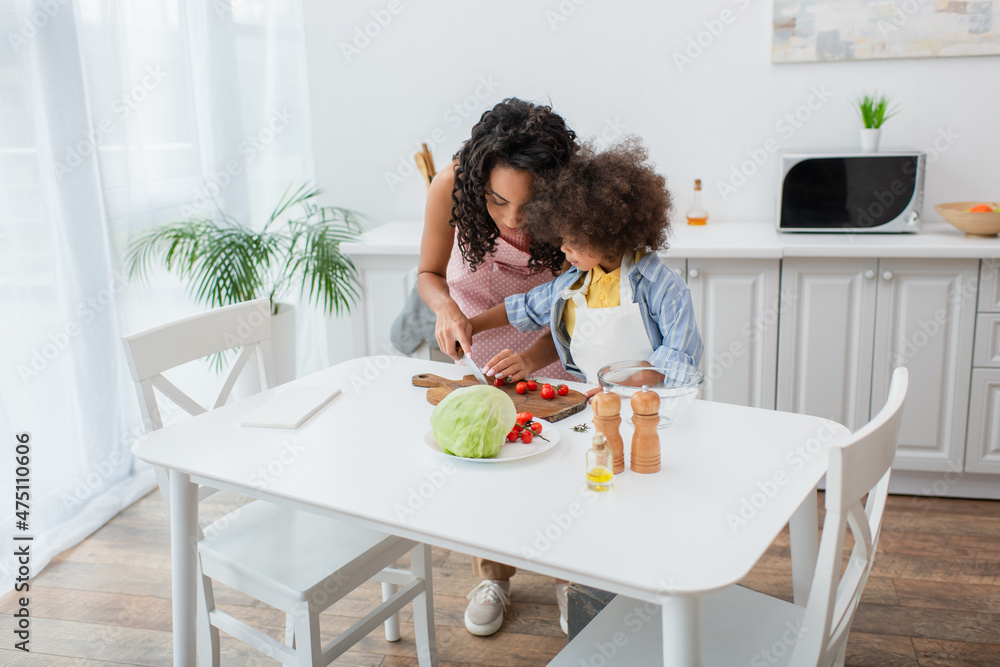 African american family cutting cherry tomatoes near oil and cabbage in kitchen.