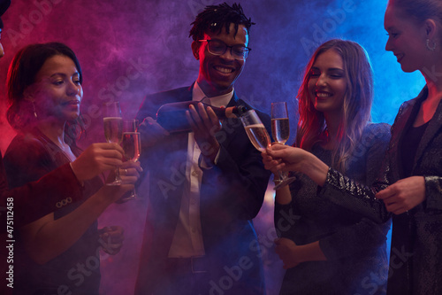 Group of cheerful young people pouring champagne in smoky nightclub while enjoying party