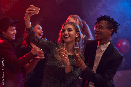Beautiful mixed-race couple taking selfie photo on dnce floor while enjoying party in night club