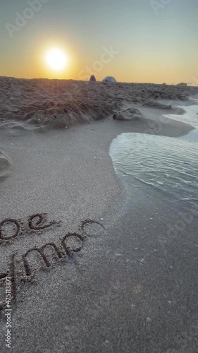 Seascape with sailboat on the shore at sunrise.	The words Good Morning are written on the sea sand , the waves are running on the deserted beach
