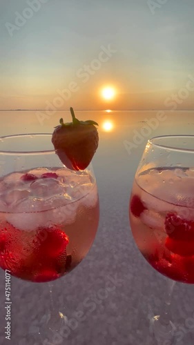 Two glasses of iced strawberry cocktail on the sea sand on romantic party at sunset	