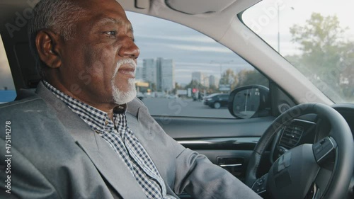 Old african american man driving car serious pensive elderly male leaves parking lot mature businessman looking closely at road drives up approaches intersection experienced driver ride on highway