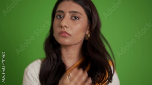 Pensive traditional Indian woman correcting her appearance at the camera in the green studio photo