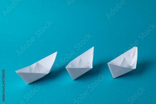 Handmade white paper boats on light blue background.  Origami art