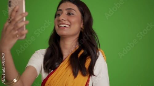 Smiling traditional Indian woman talking by video call on phone in the green studio photo