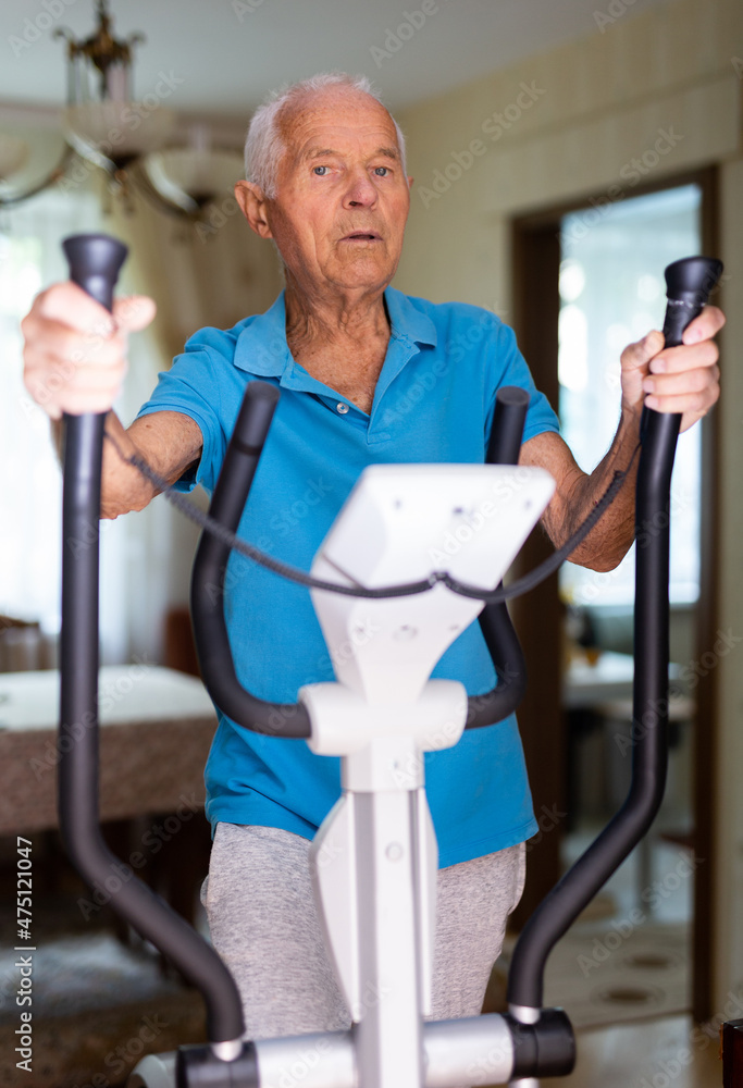 Old man using elliptic trainer at home Old man using elliptic trainer at home