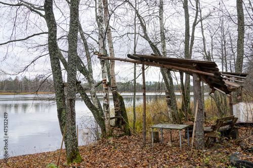 abandoned house in the woods camp of fishermen hunters on the shore of the lake in the autumn forest. broken roof and wooden bench. Homemade boat . High quality photo © Lunatishe