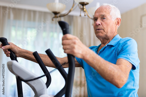 Elderly man exercising on elliptic trainer in living room