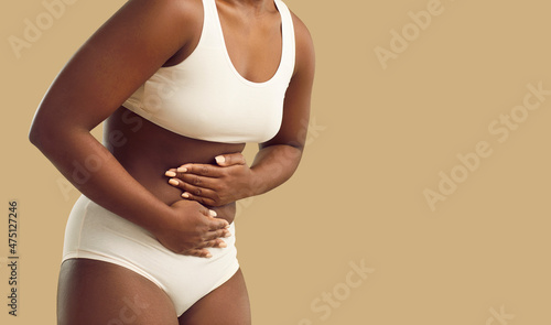 Crop shot of unhealthy African American woman on yellow studio background suffer from stomachache. Pain in belly or abdomen. Sick ethnic girl struggle with pms or gastritis. Healthcare concept. photo