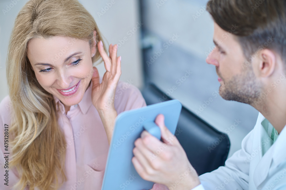 Man showing mirror and woman trying on hearing aid