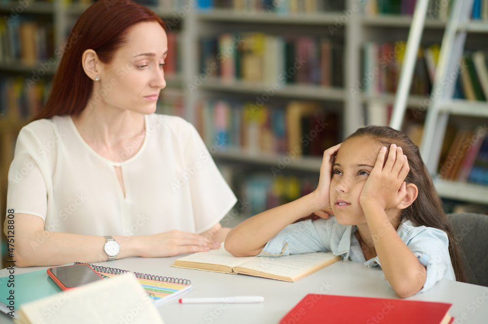 Sad girl and young woman studying at table Sad girl and young woman studying at table