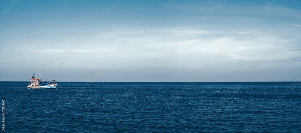 A fishing boat floats alone in the calm sea. The sky background above the horizon for copy space. Ocean nature landscape. The vessel is on the water.