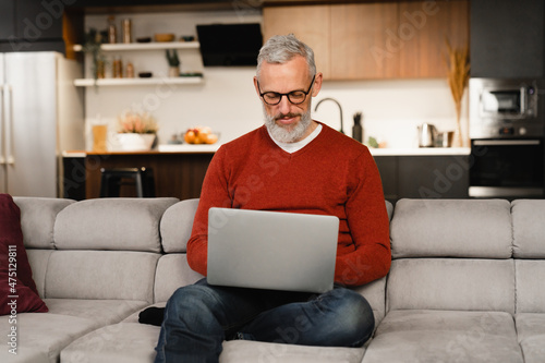 Relaxed caucasian mature middle-aged man working at home on laptop remotely on distance online, watching webinars, checking e-mails, e-learning on lockdown © InsideCreativeHouse
