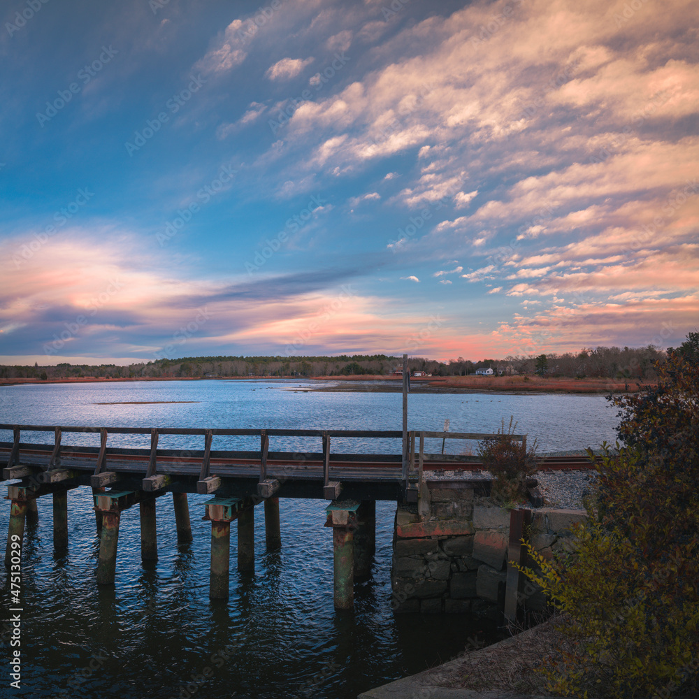 Fototapeta premium Beautiful sunrise seascape with the view of old railroad bridge and dramatic clouds along coastal village in Wareham, Massachusetts. Travel landscape theme for New England, train, trip, or nostalgia.