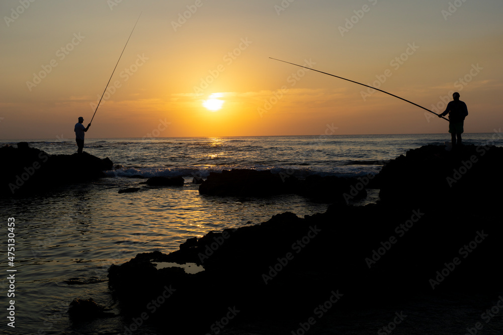 Silhouette of two fishermen fishing  the last sun rays at the beach in Israel