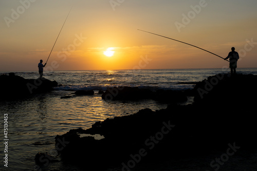 Silhouette of two fishermen fishing the last sun rays at the beach in Israel