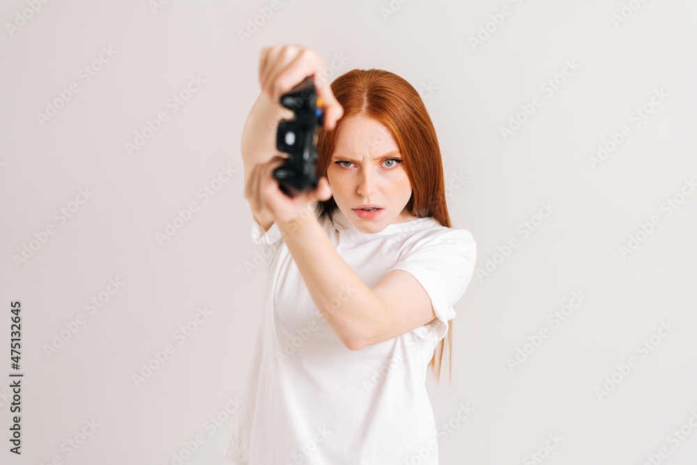 Studio portrait of focused young woman playing video game with controller looking at camera on white isolated background. Happy lady using joystick on console enjoying online game. Studio portrait of focused young woman playing video game with controller looking at camera on white isolated background. Happy lady using joystick on console enjoying online game.