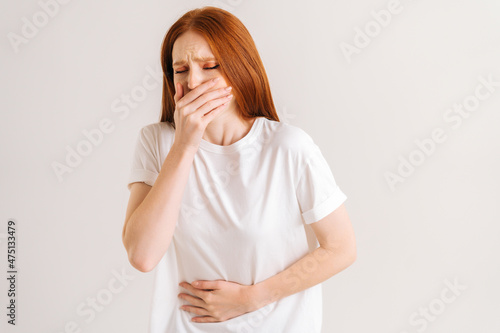 Portrait of suffering young woman feeling painful cramp in stomach, grimacing and writhing in pain feeling stomach ache indigestion, periods menstruation, on white isolated background in studio.