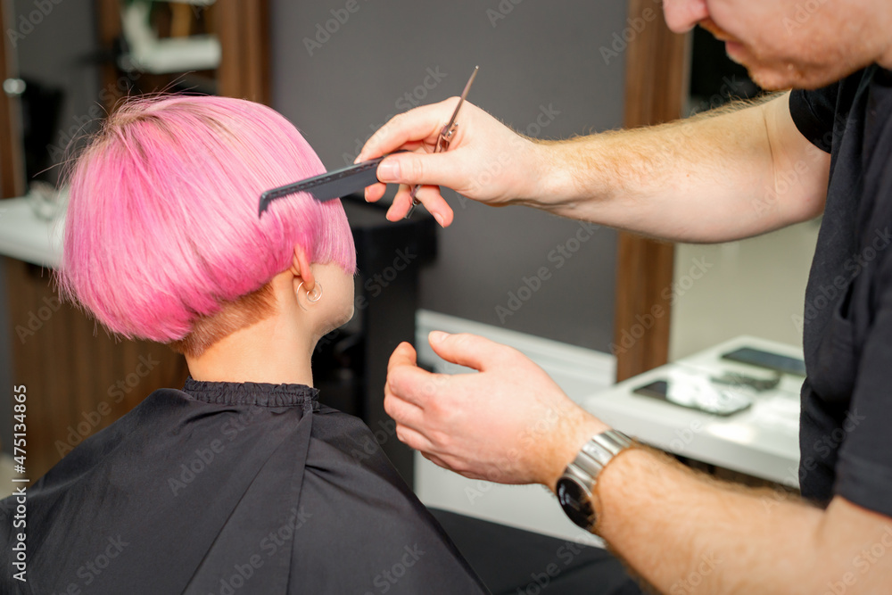 Hands of hairdresser combing hair making short pink hairstyle for a young caucasian woman in a beauty salon