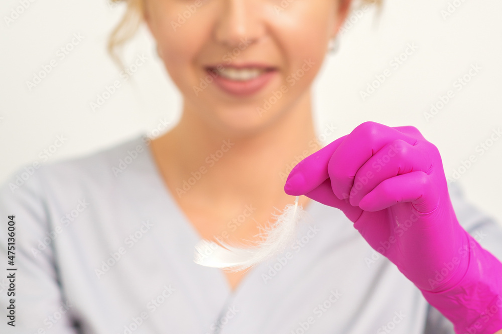 The beautician holds white feathers in her gloved hands over white background. Concept of health softness skin and body care The beautician holds white feathers in her gloved hands over white background. Concept of health softness skin and body care