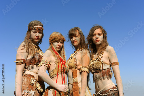 A Group of women are dressed as Neanderthal warriors. Their bodies and faces are covered with mud, filth and dirt. 