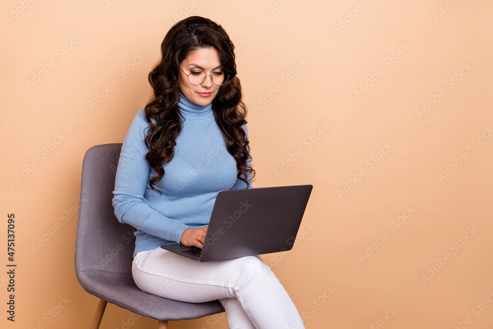 Photo of sweet serious lady dressed blue pullover glasses typing device empty space isolated beige color background Photo of sweet serious lady dressed blue pullover glasses typing device empty space isolated beige color background
