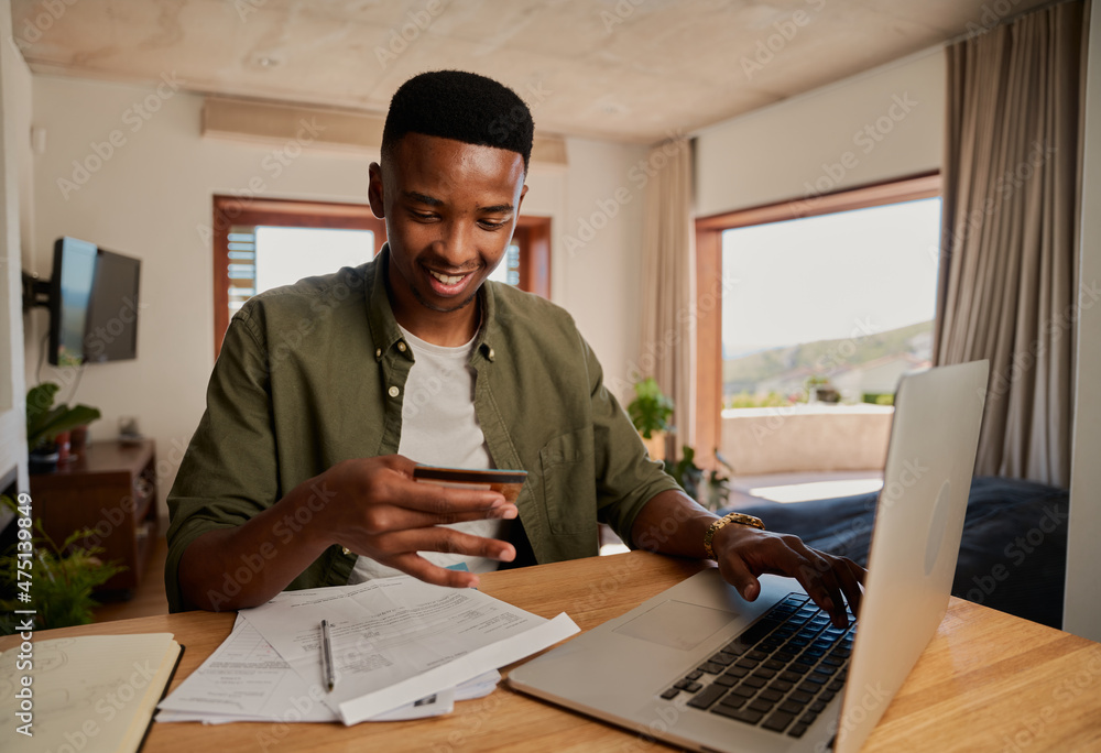 Happy young adult black male smiling, making online payment on laptop in modern apartment. Happy young adult black male smiling, making online payment on laptop in modern apartment.