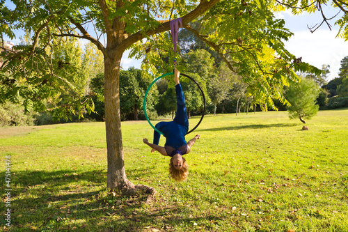 Blonde woman and young gymnast acrobat athlete performing aerial exercise on air ring outdoors in park. Lithe woman in blue costume performs poses of circus performers dancing with hips