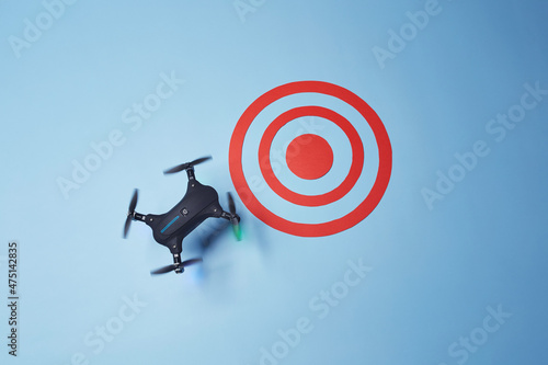 Aerial top down view on isolated drone copter with spinning propellers reaching the red target on the bright solid blue fond background