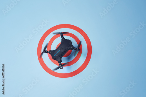 Aerial top down view on isolated drone copter with spinning propellers flying above the reached red target on the bright solid blue fond background